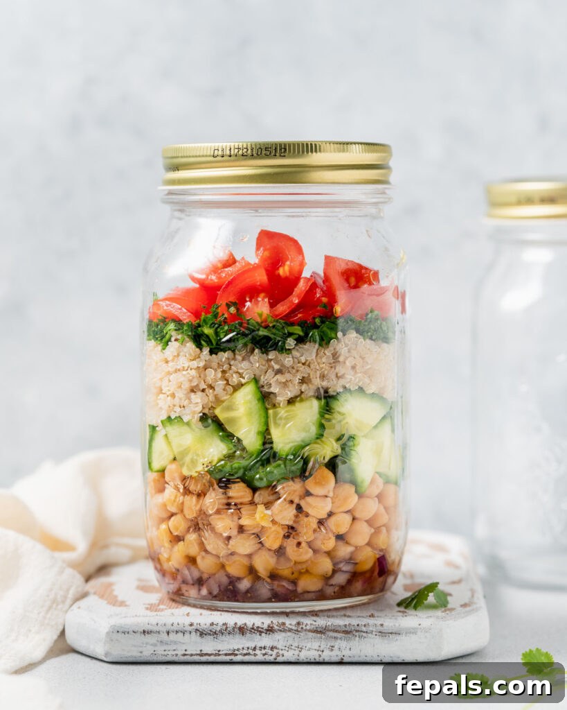 Refreshing Layered Chickpea Cucumber Jar 12 A side view of a layered salad jar, showcasing chickpeas, cucumber, quinoa, fresh parsley, and tomatoes, sealed with a lid.