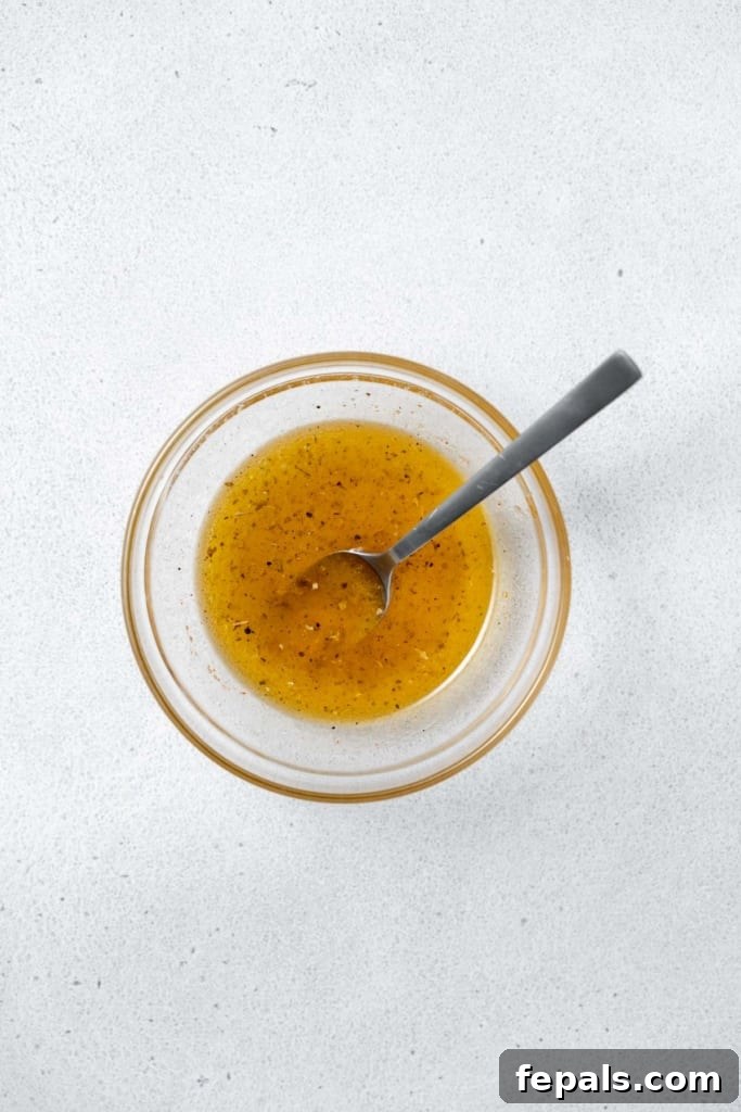 Refreshing Layered Chickpea Cucumber Jar 5 A hand mixing a vibrant vinaigrette dressing in a small glass bowl with a whisk.