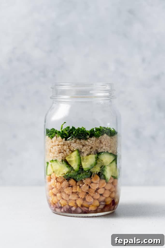 Refreshing Layered Chickpea Cucumber Jar 8 Progress shot of a salad jar being assembled, showing layers of dressing, chickpeas, cucumber, quinoa, and fresh herbs.