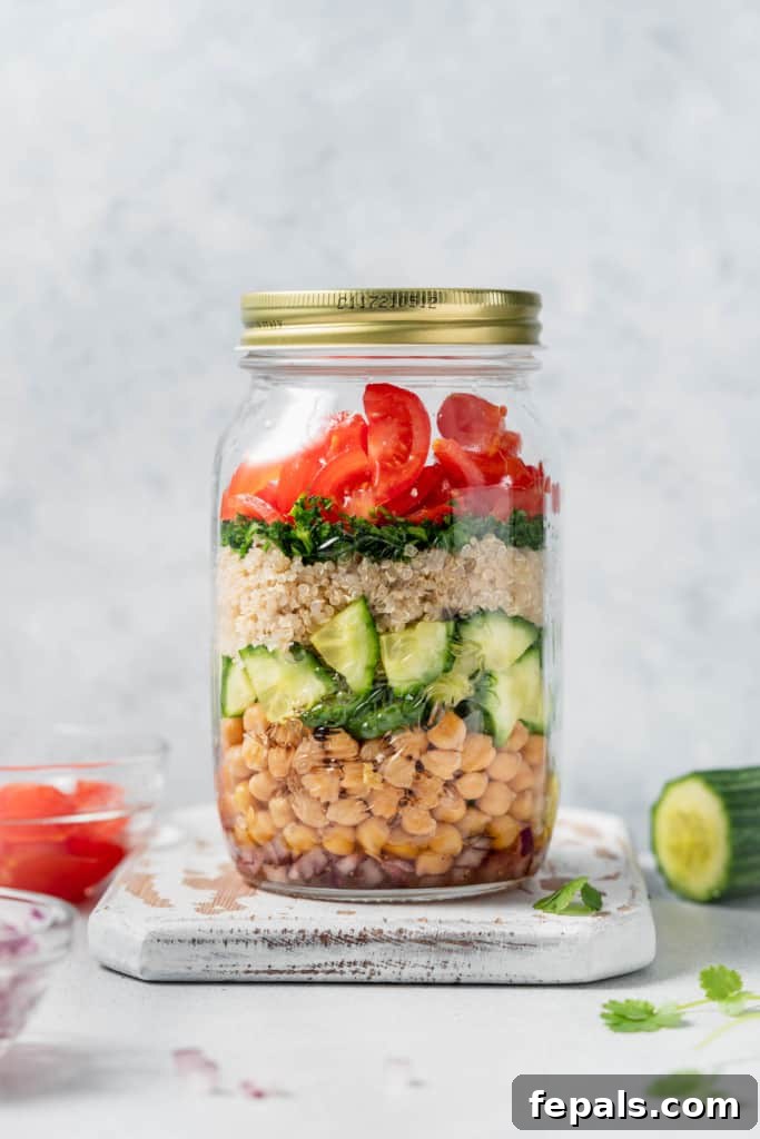 Refreshing Layered Chickpea Cucumber Jar 10 A chickpea quinoa salad jar resting beside freshly chopped cucumber and tomatoes, highlighting its fresh ingredients.