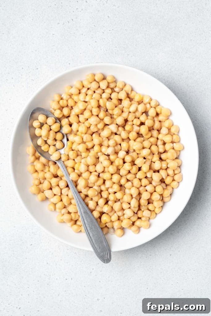 Your Guide to Perfectly Cooked Chickpeas 11 Cooked chickpeas in a white bowl with a spoon.