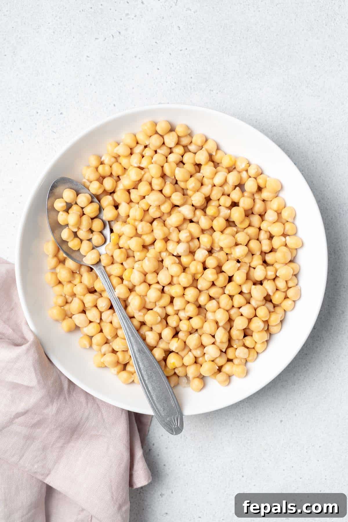 Your Guide to Perfectly Cooked Chickpeas 12 Spoon on a white bowl filled with chickpeas.