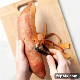 hand holding a sweet potato and another hand peeling the sweet potato with a peeler