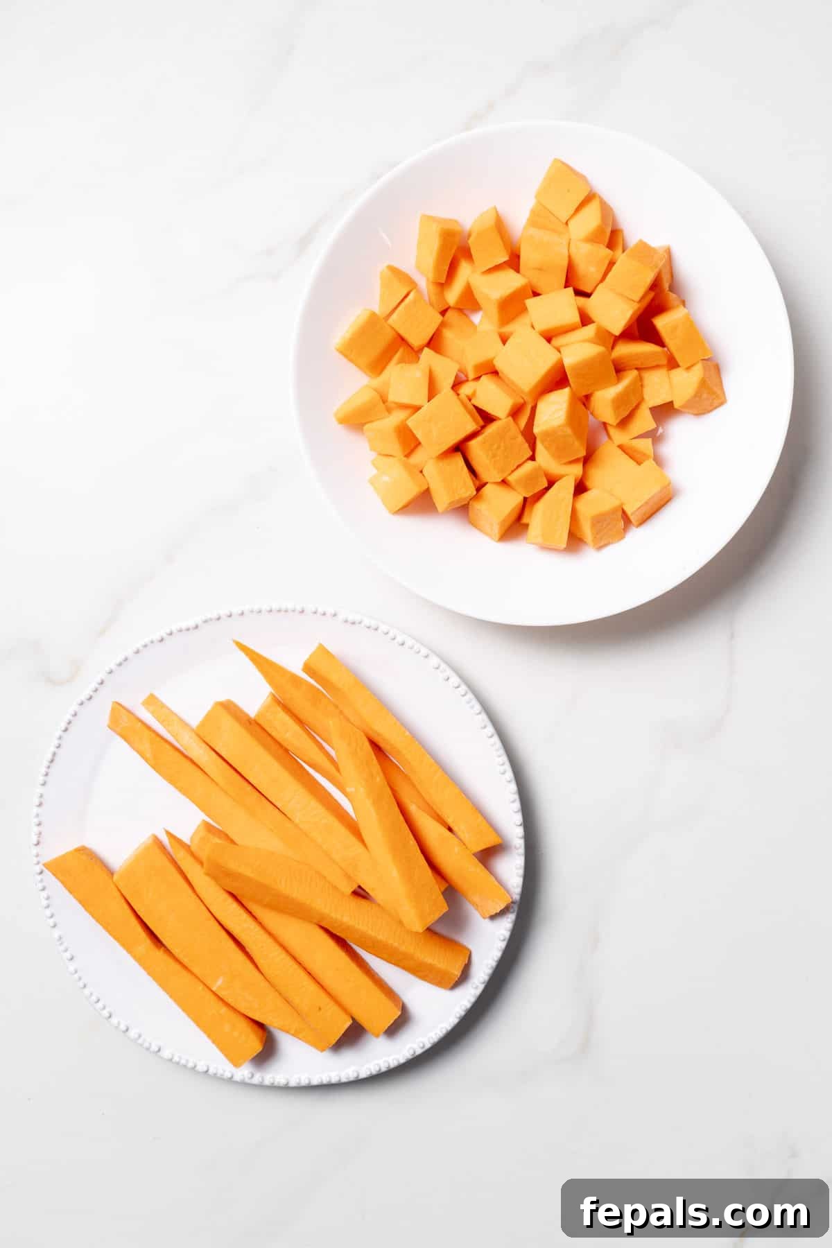 Sweet potato cut into cubes and sticks on two white plates.