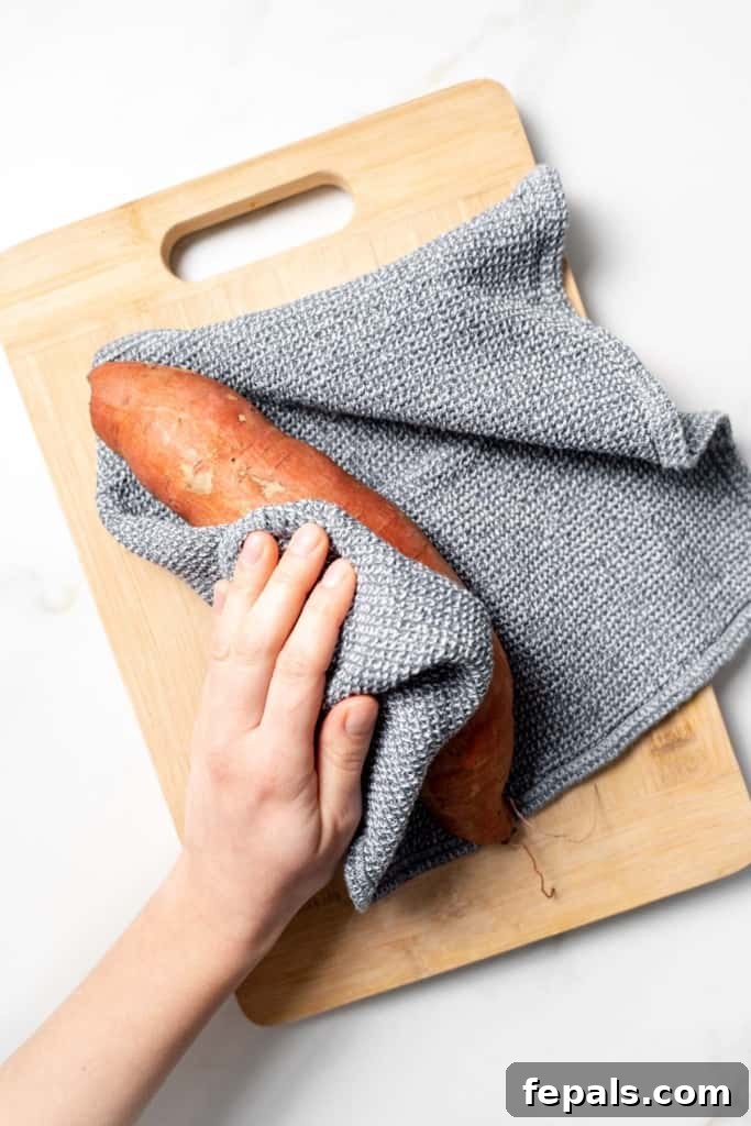 Patting a sweet potato dry with a kitchen towel.