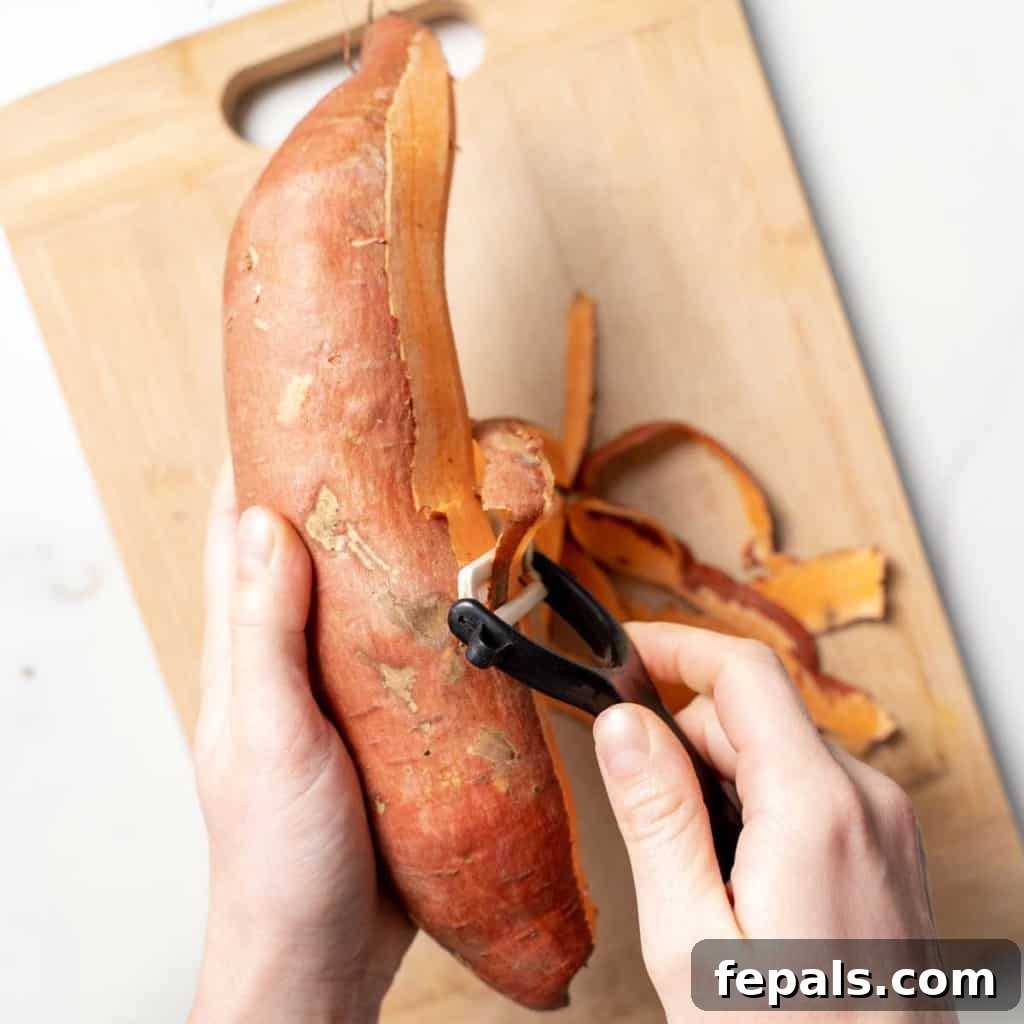 hand holding a sweet potato and another hand peeling the sweet potato with a peeler