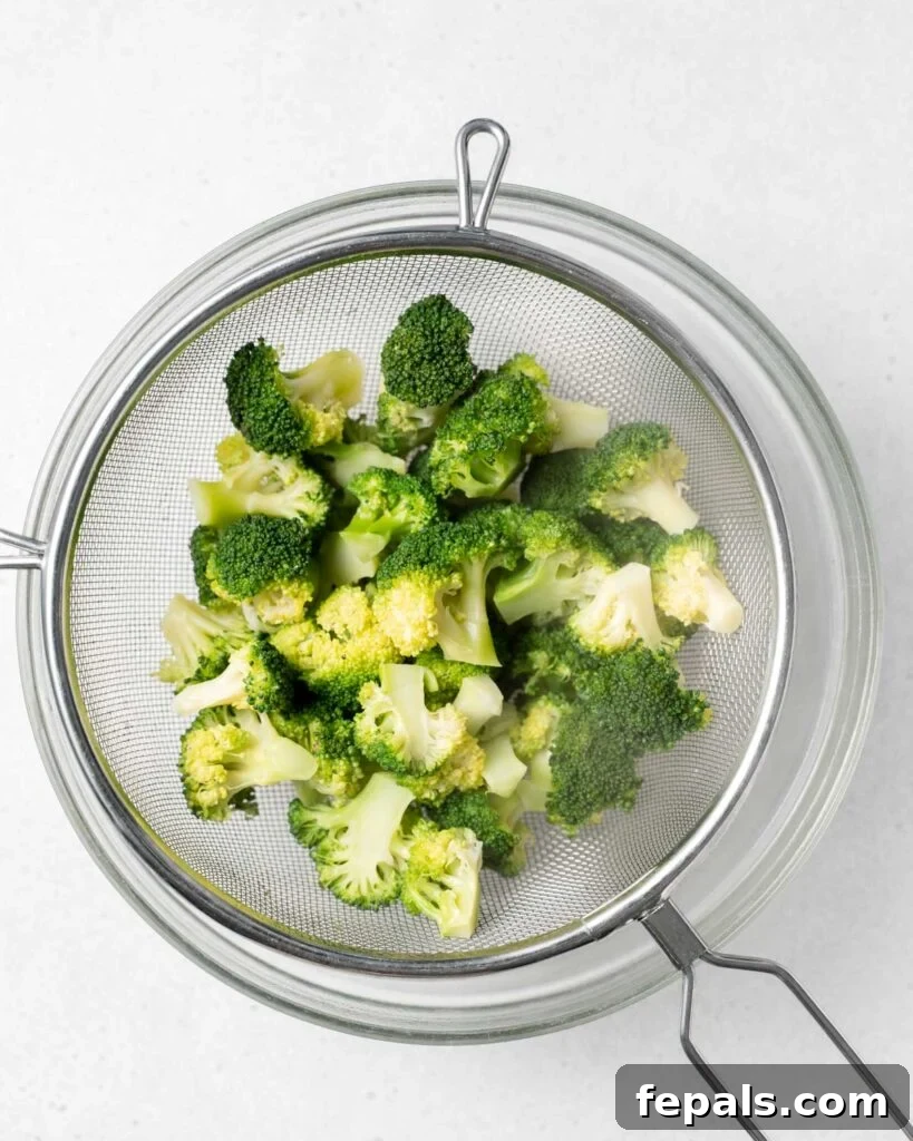 Stovetop Broccoli Perfection 14 Cooked broccoli florets being transferred from a sifter into an ice bath, demonstrating the shocking process.