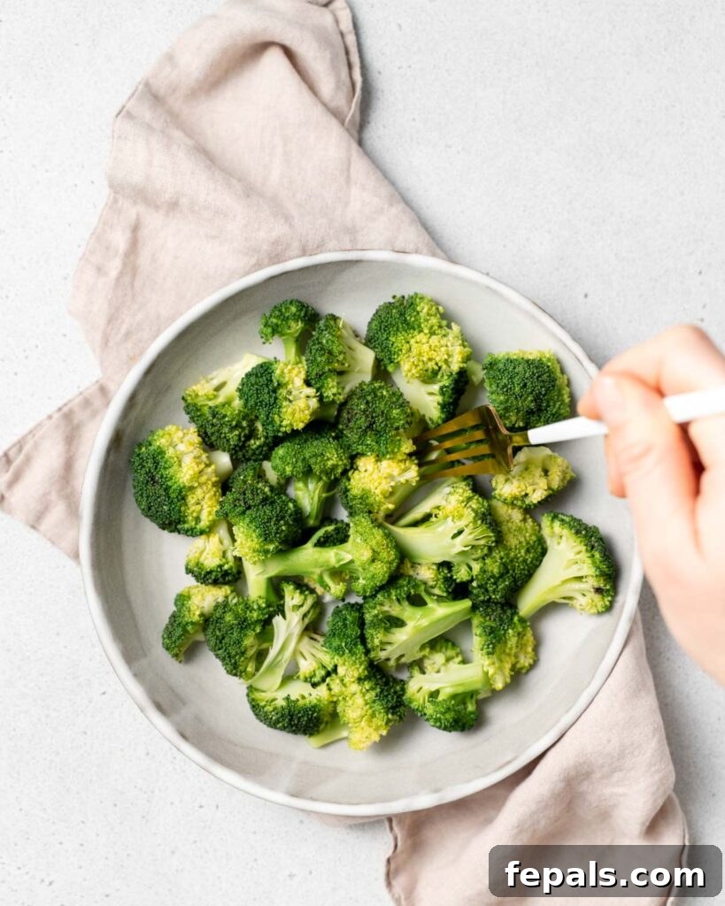 Perfect Stovetop Broccoli 16 hand holding fork grabbing a piece of cooked broccoli floret from a plate