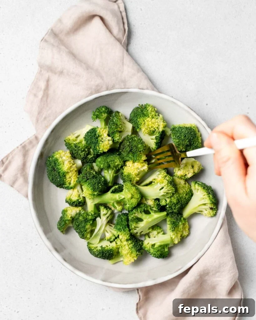 Stovetop Broccoli Perfection 16 A hand holding a fork, grabbing a piece of perfectly cooked broccoli floret from a white plate.