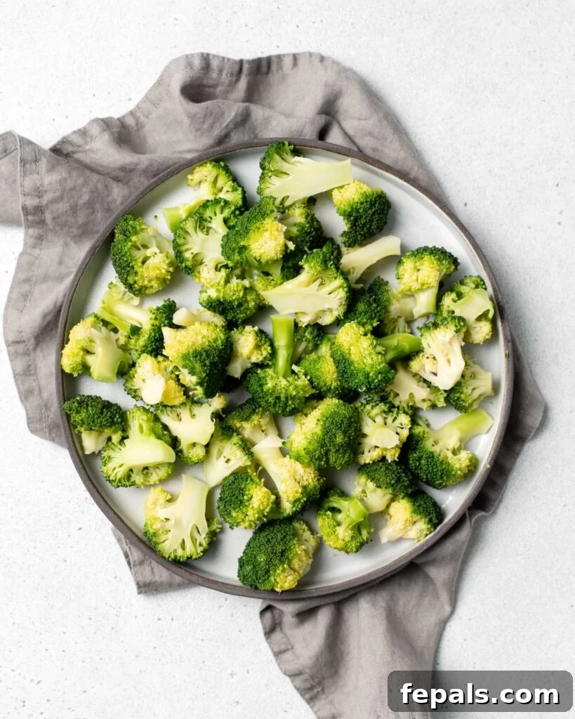 Stovetop Broccoli Perfection 18 Top view of vibrant green, cooked broccoli florets beautifully arranged on a round white plate, resting on a gray cloth napkin.