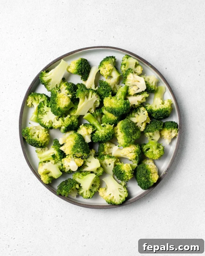 Stovetop Broccoli Perfection 4 Top view of vibrant green, cooked steamed broccoli florets artfully arranged on a round white plate.