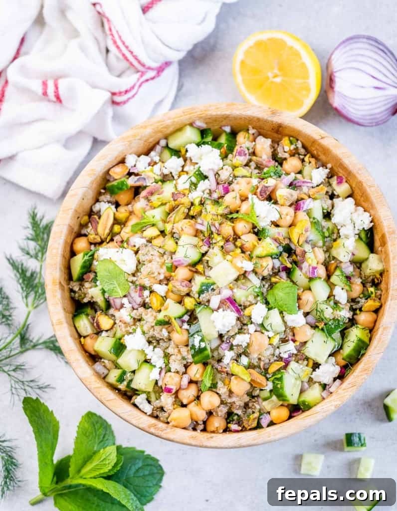 Top view green salad with chickpeas topped with crumbled cheese in a wooden bowl.