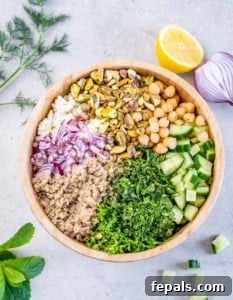 Herbs, cucumber, quinoa, chickpeas and pistachios added to a large wooden bowl.