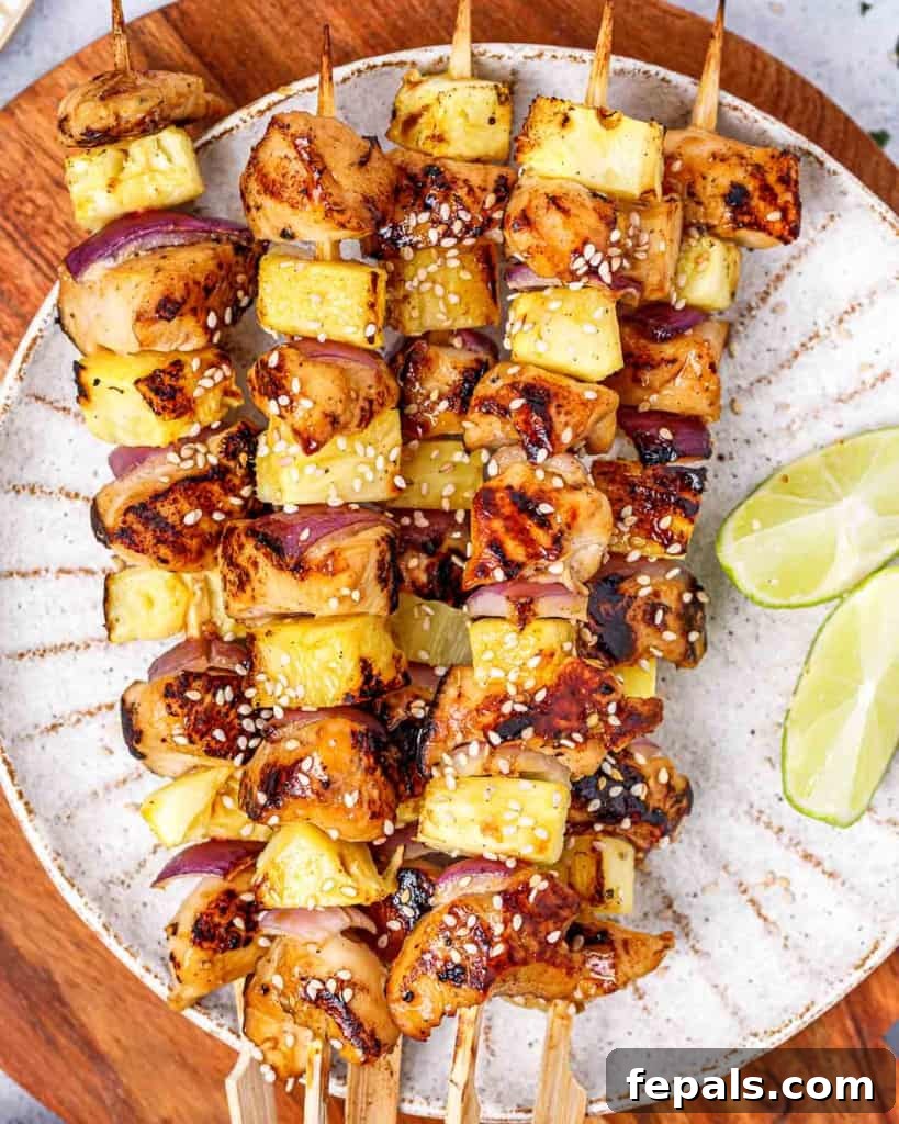 Grilled Umami Chicken Skewers 12 Top view of chicken skewers with pineapple and red onion on a white plate, ready to be served.