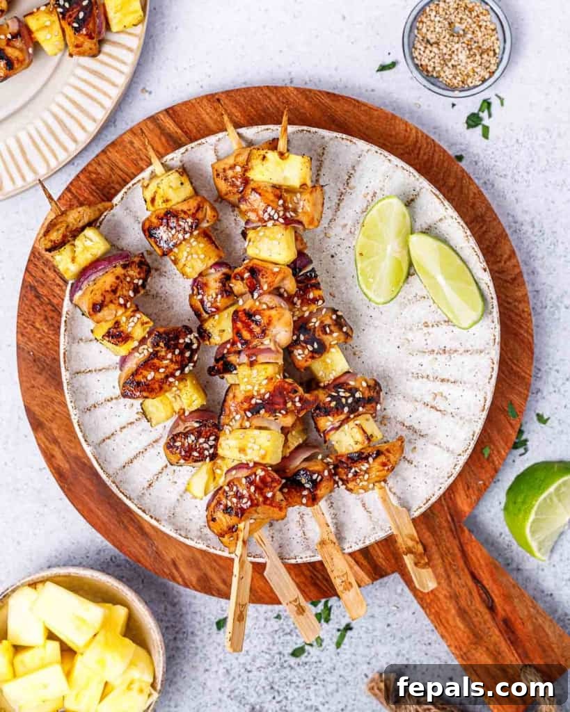 Grilled Umami Chicken Skewers 3 Grilled teriyaki chicken skewers made with pineapple and red onion on a white plate, ready to be served.