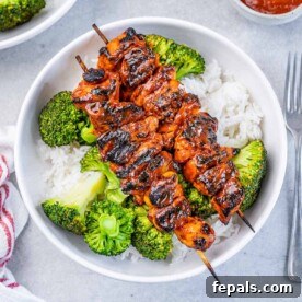 top view of 2 grilled chicken skewers over a bowl of rice with steamed broccoli