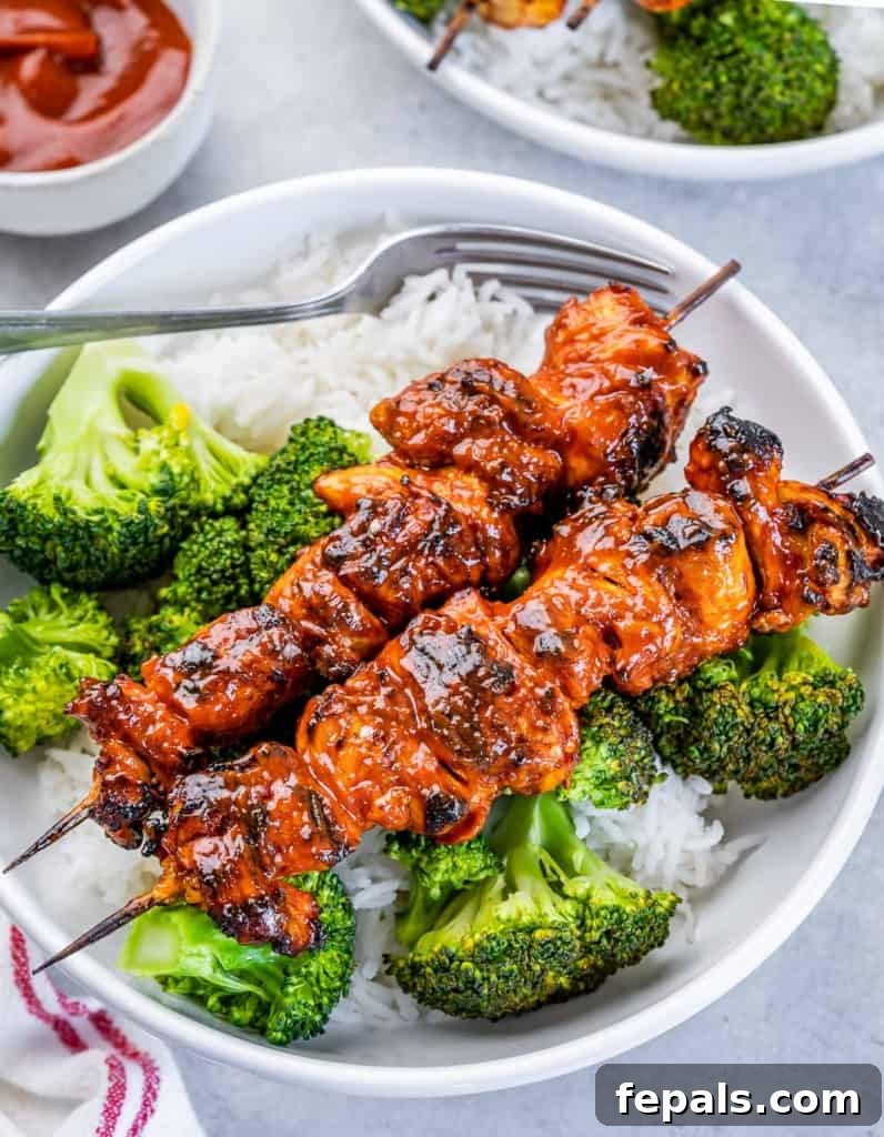 side shot of 2 chicken kabobs over rice and broccoli in a round white bowl