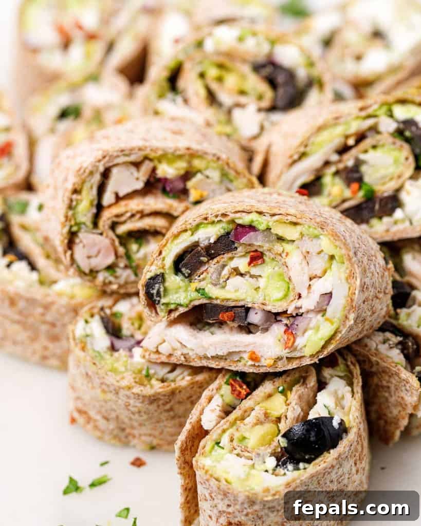 Several avocado chicken salad pinwheels neatly stacked on a white plate, ready to be served.