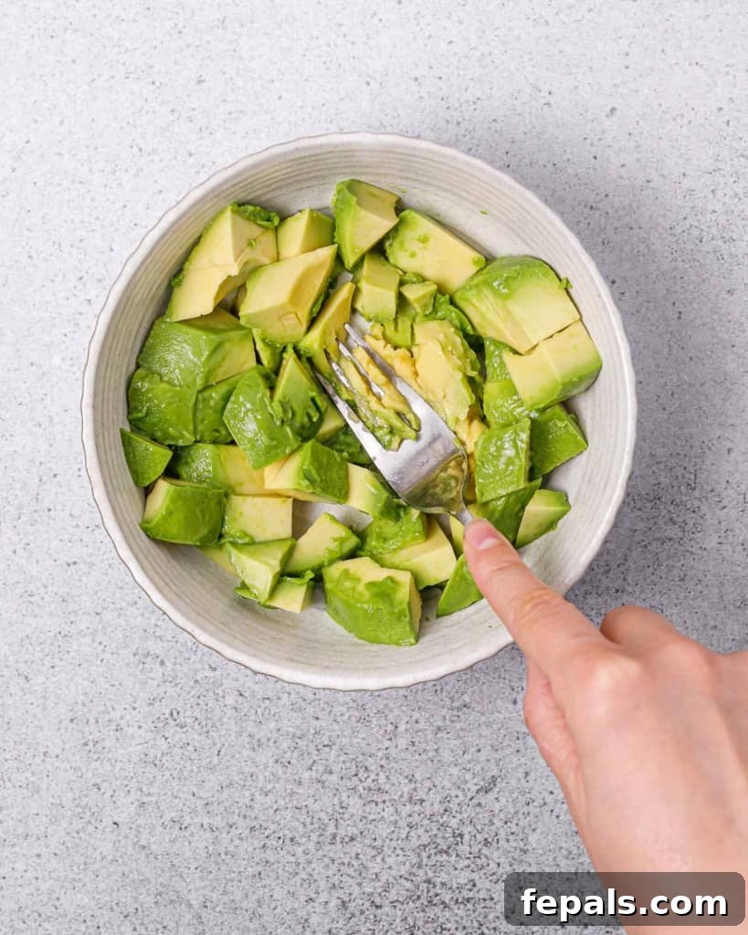 Mashing a ripe avocado in a white bowl using a fork to create a smooth, creamy base for the spread.