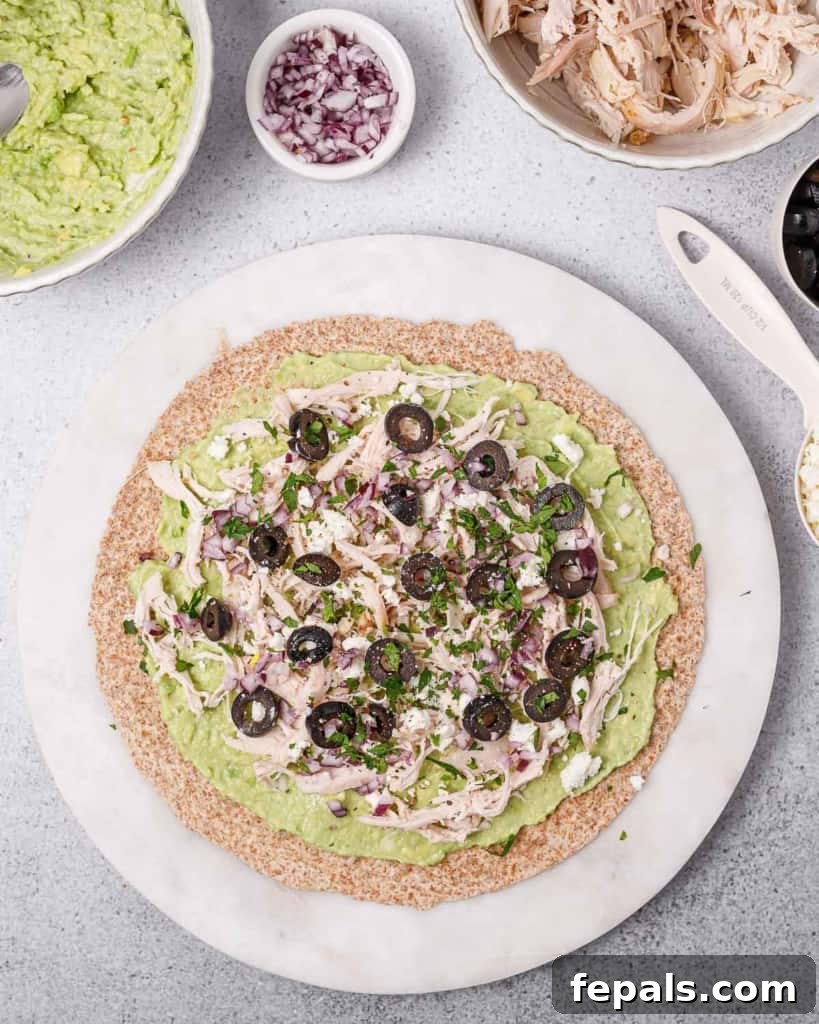 Topping a tortilla with shredded chicken, black olives, and crumbled feta cheese, preparing for the next layer of flavor.