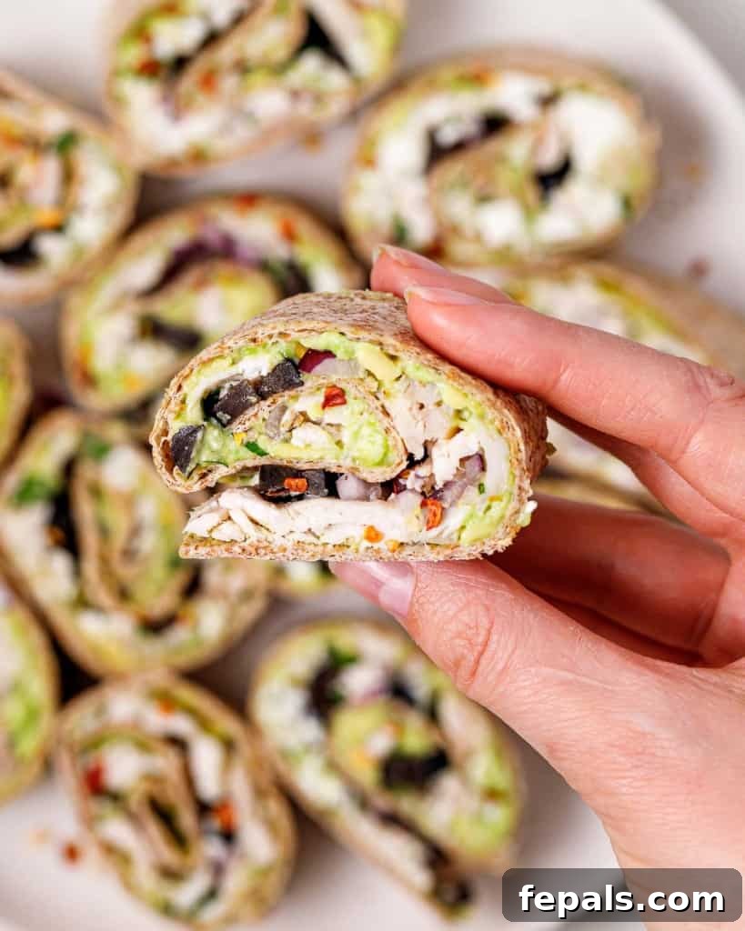 A woman's hand delicately holding a single, perfectly sliced tortilla pinwheel, ready to be enjoyed.