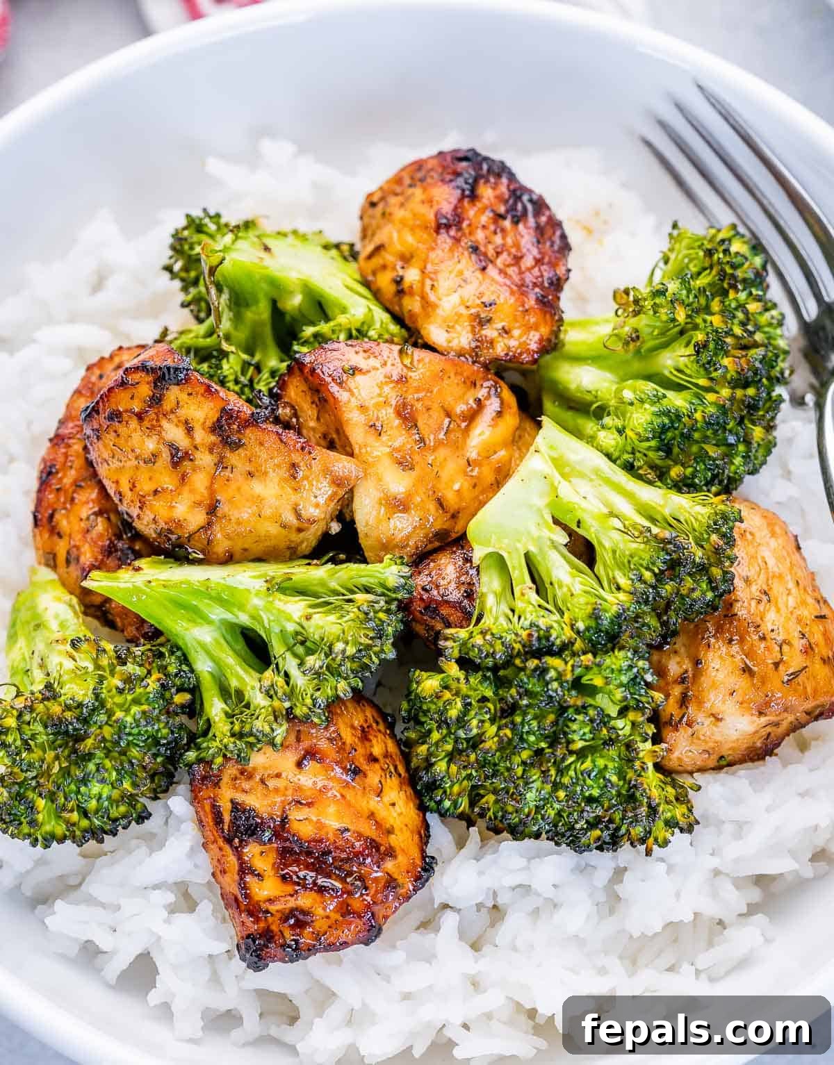 A close-up view of perfectly cooked chicken and vibrant green broccoli florets nestled over a bed of fluffy white rice, ready to be enjoyed.