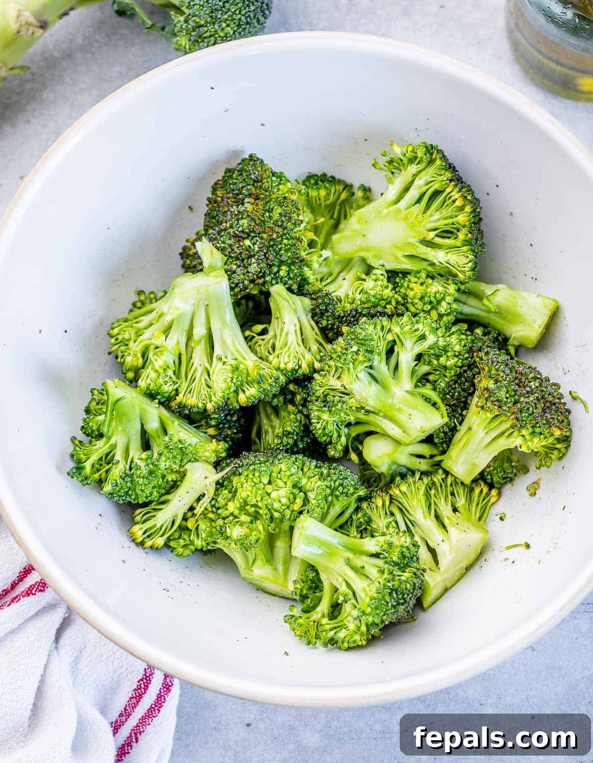 Freshly cut broccoli florets, lightly seasoned and ready for cooking, displayed in a round white bowl.