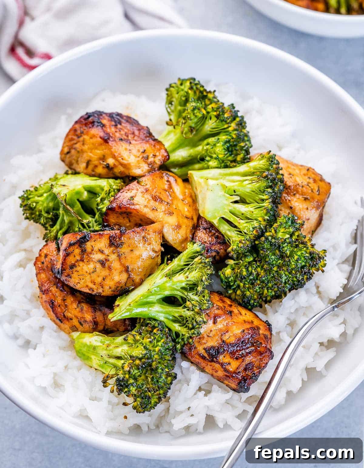 A serving of air fryer chicken and broccoli beautifully arranged over white rice in a pristine white bowl, ready to be enjoyed.