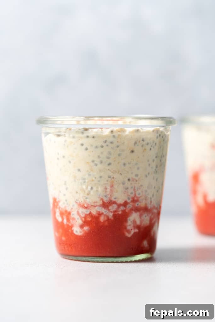 Layering overnight oats over strawberry puree in a jar.