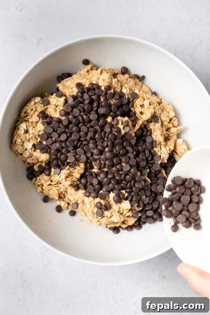 Pouring chocolate chips into a bowl with oat peanut butter mixture, adding the final flavor.