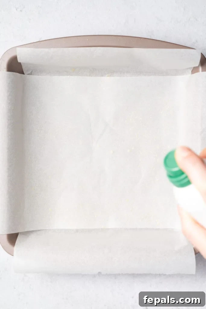 Spraying cooking spray on parchment paper in a pan, preparing for the mixture.