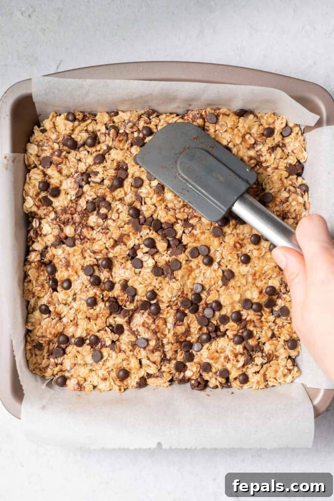 Using a spatula to spread and press the peanut butter oatmeal bar mixture evenly in a pan.