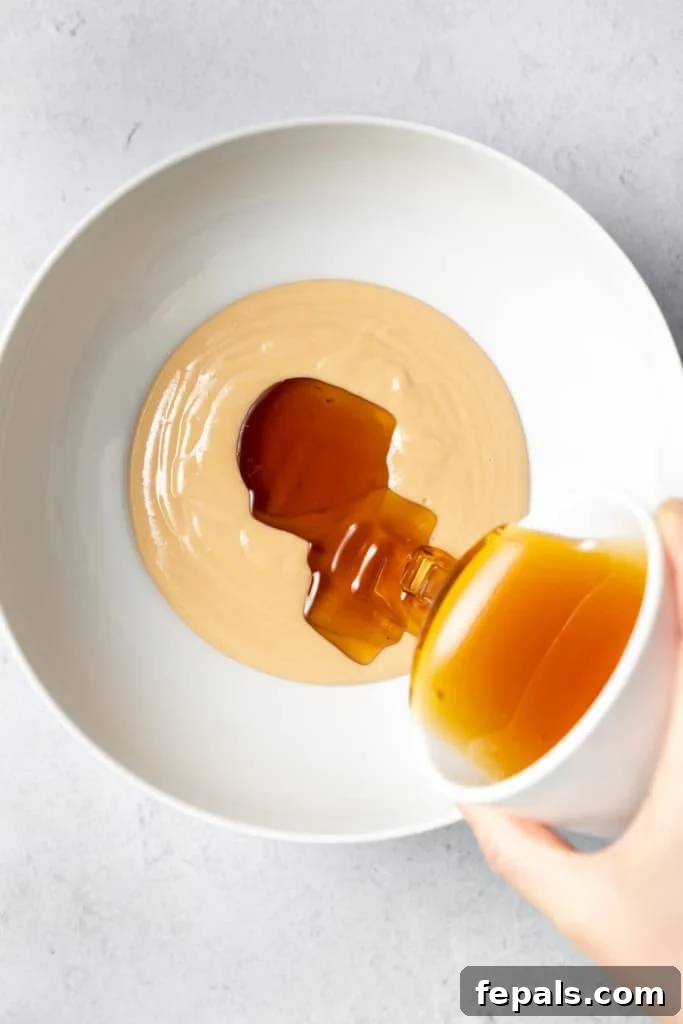 Adding honey to peanut butter in a white bowl, preparing for the mixture.