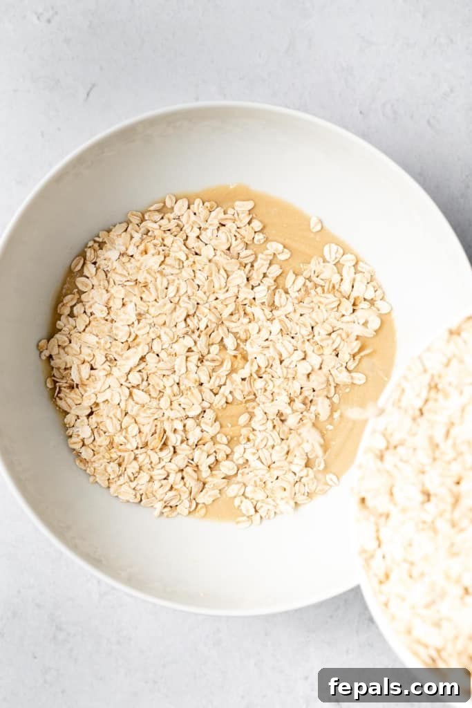 Adding oats to the peanut butter mixture, beginning the combination process.