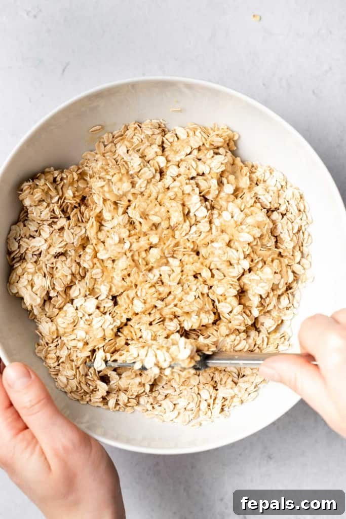 Using a spatula to stir oats into the peanut butter and honey mixture, ensuring full coating.