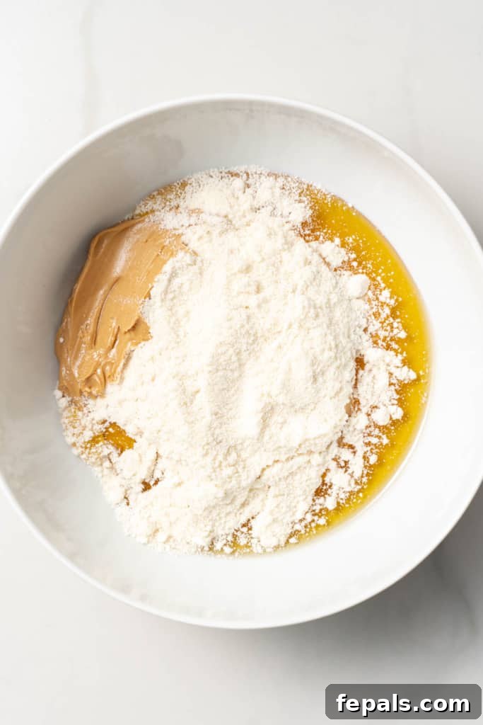 Adding coconut flour to a bowl with honey and peanut butter.