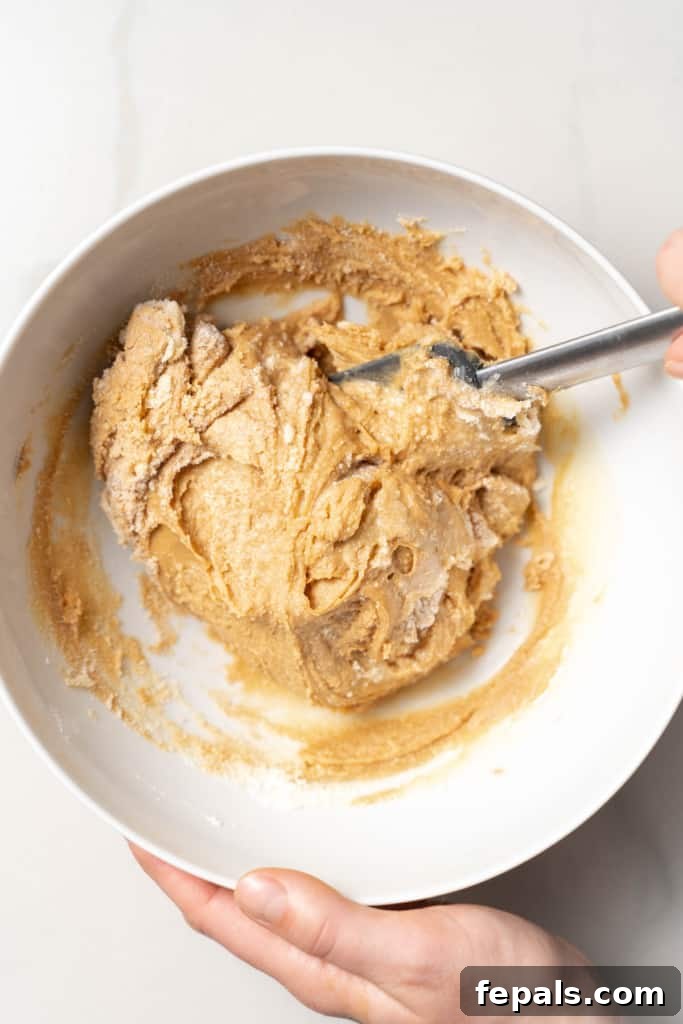 Stirring peanut butter, honey and coconut flour in a white bowl.
