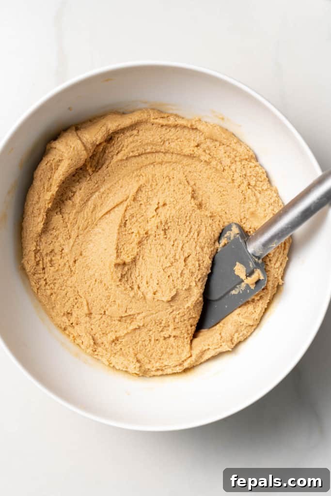 Using a spatula to stir peanut butter, honey and coconut flour.