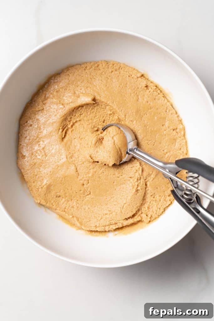 Scooping peanut butter dough out of a white bowl.