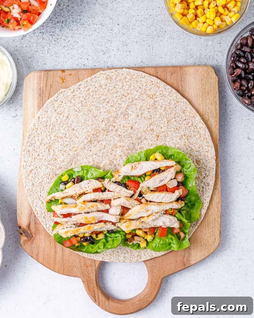Spicy Southwest Chicken Wrap 10 Succulent grilled chicken slices generously added over the vibrant layers of lettuce, black beans, corn, and pico de gallo on a tortilla wrap, completing the filling process.