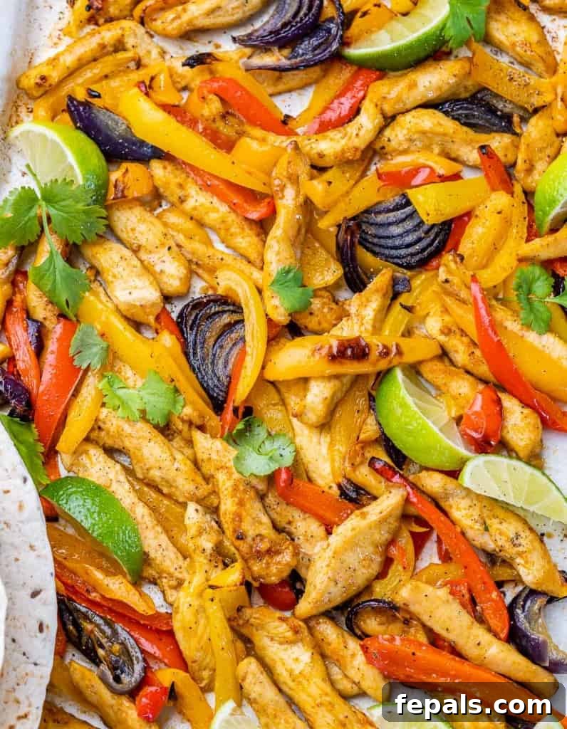 Chicken fajitas with bell peppers, onion and lime wedges on a sheet pan.