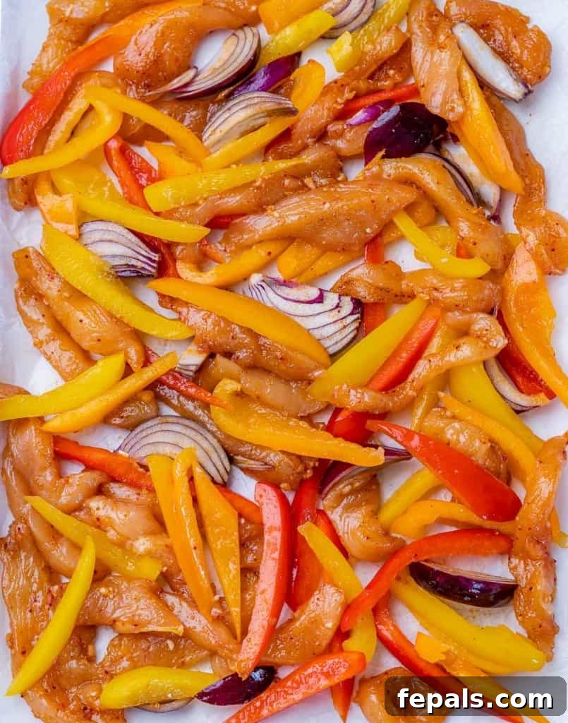 Placing marinated chicken strips and veggies on a sheet pan.