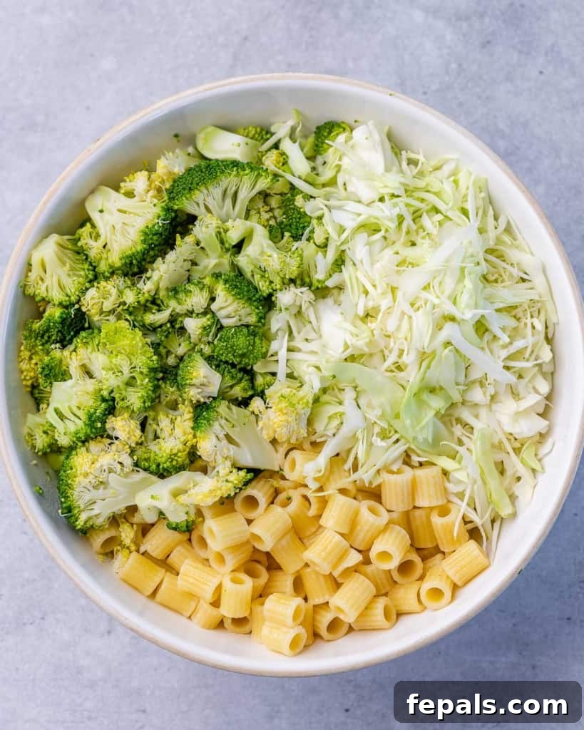 Zesty Green Goddess Pasta Salad 6 Cooked pasta, chopped cabbage, and chopped broccoli in a round white bowl, ready for dressing.