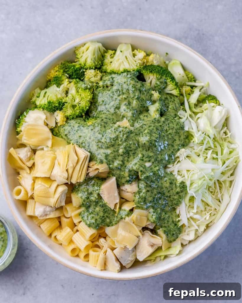 Zesty Green Goddess Pasta Salad 7 Green Goddess pesto sauce being added over a bowl of pasta, broccoli, and shredded cabbage.