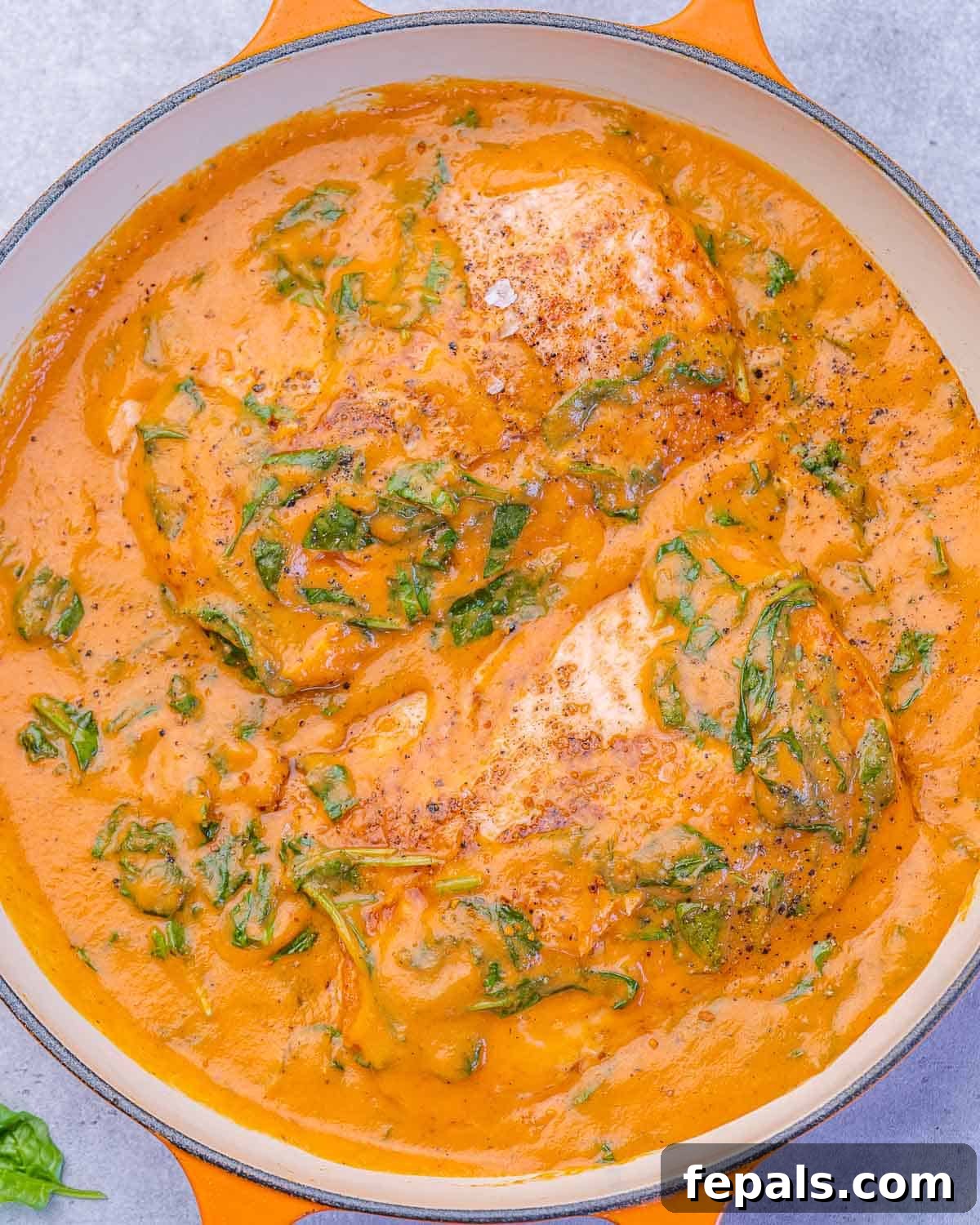 Overhead shot of salmon cooking in a thick spinach and roasted red pepper sauce, garnished with fresh herbs.