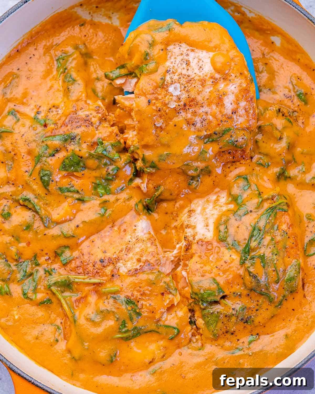 Close-up of salmon fillets in a creamy spinach and roasted red pepper sauce, bubbling in a skillet, garnished with parsley.