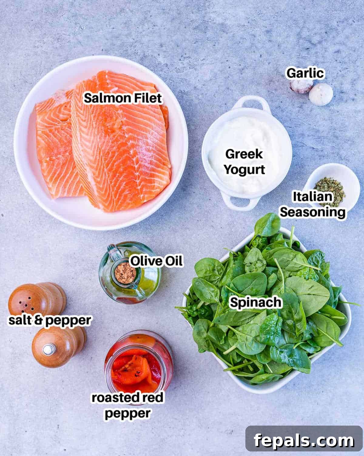 A selection of fresh ingredients including salmon, spinach, roasted red peppers, garlic, and Greek yogurt on a wooden board.