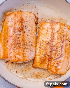 Two salmon fillets searing in a skillet until golden brown on the outside.