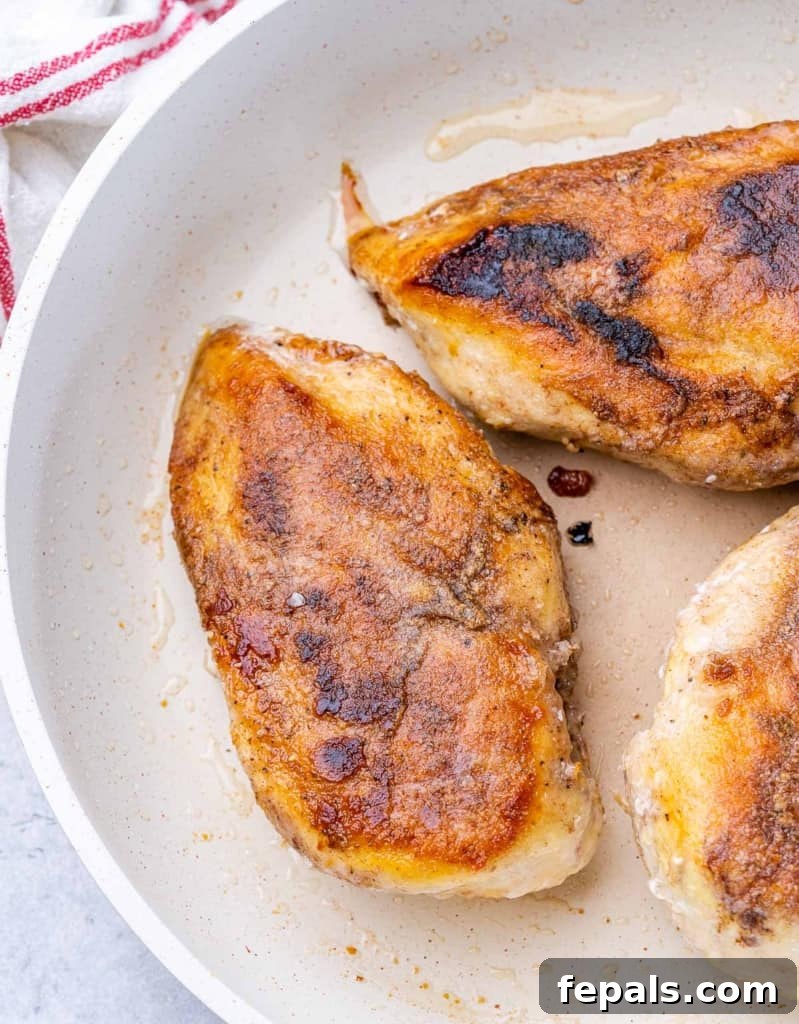 Sticky Honey Sriracha Chicken 6 Seared chicken breast cooking in a pan, showing a golden-brown crust.