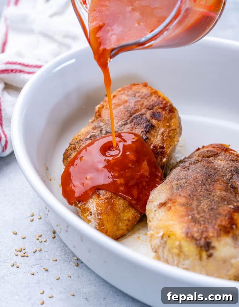 Sticky Honey Sriracha Chicken 7 Honey sriracha sauce being poured generously over seared chicken in a baking dish, ready for the oven.